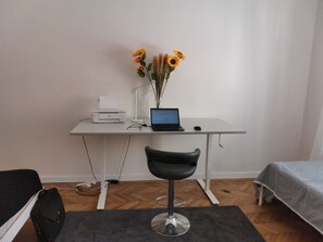 A small, modern room with a desk, laptop, printer, and a chair. There is a bed with a grey bedspread and a small table with a lamp. - Downtown 3 BDR Charm - walk to all attractions (Bratislava)