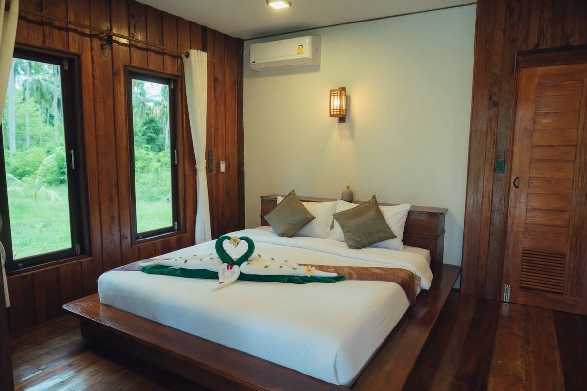 Een slaapkamer met een houten frame, een bed, kussens en een hartvormige decoratie op het bed.