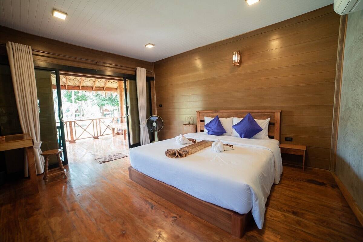 Een slaapkamer met houten lambrisering, een groot bed, twee nachtkastjes en een ventilator.