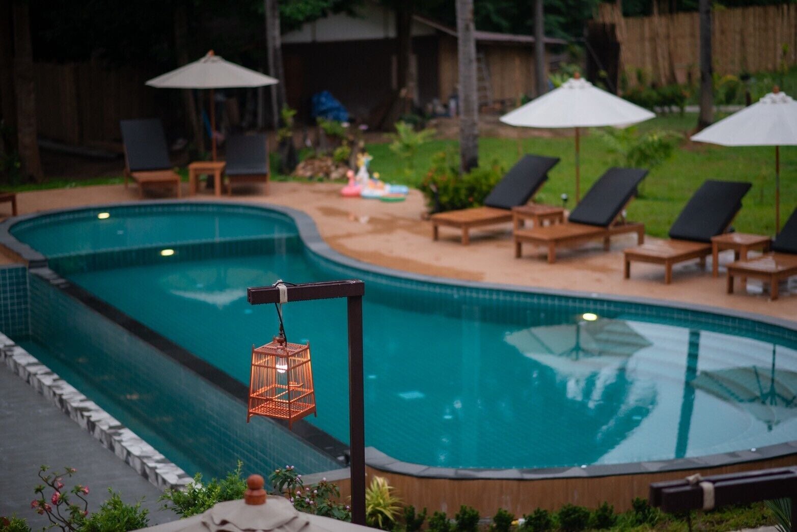 A swimming pool with lounge chairs and umbrellas, surrounded by greenery.