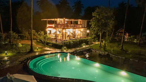 Ein zweistöckiges Gebäude mit Pool und Außenbereich zum Sitzen, umgeben von Palmen und viel Grün.