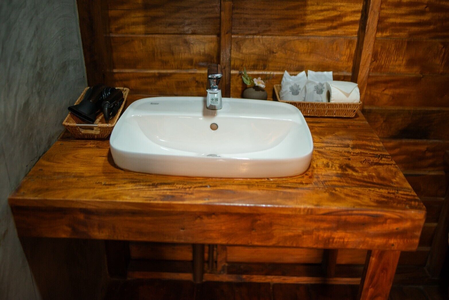 Un baño con tocador de madera, un lavabo blanco y una pequeña cesta con artículos de aseo.