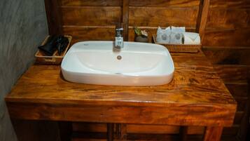 Un baño con tocador de madera, un lavabo blanco y una pequeña cesta con artículos de aseo.