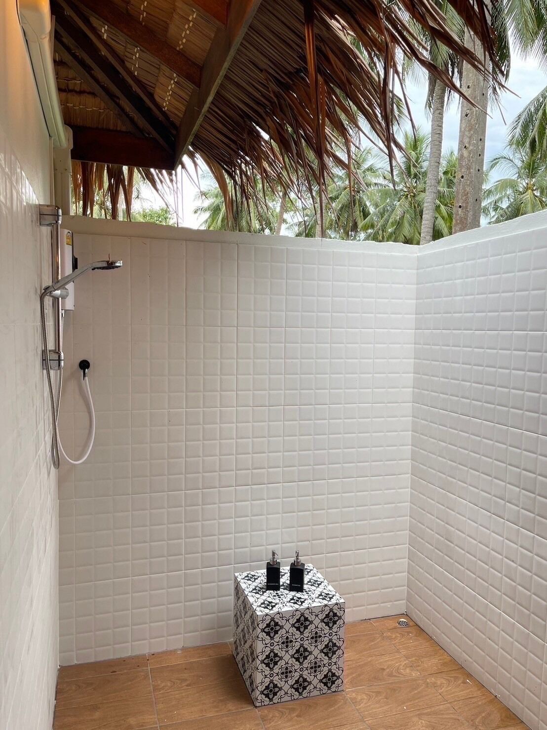 Une petite salle de douche carrelée, équipée d’une pomme de douche et d’un pommeau de douche amovible. Un petit tabouret à motifs se trouve dans un coin.