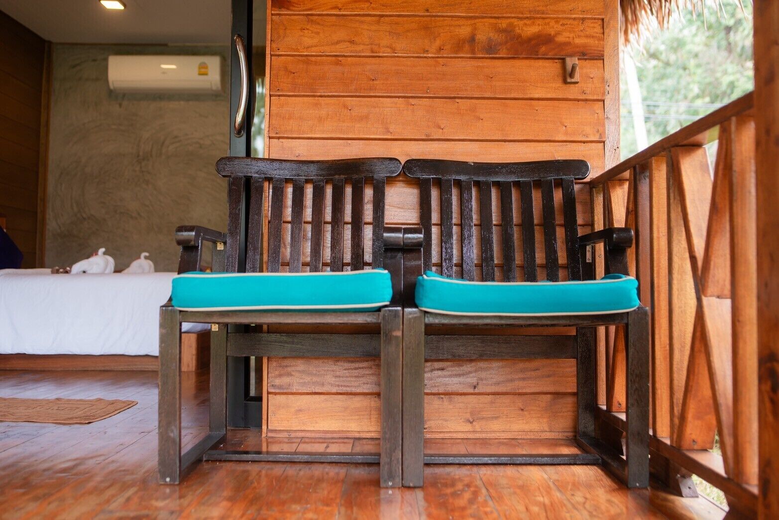 A wooden bench with turquoise cushions in a room with wooden walls and a bed in the background.