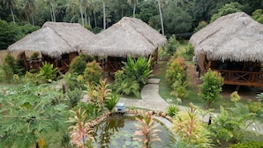 Ein tropisches Resort mit strohgedeckten Hütten, einem Teich mit Seerosen und üppiger Vegetation.