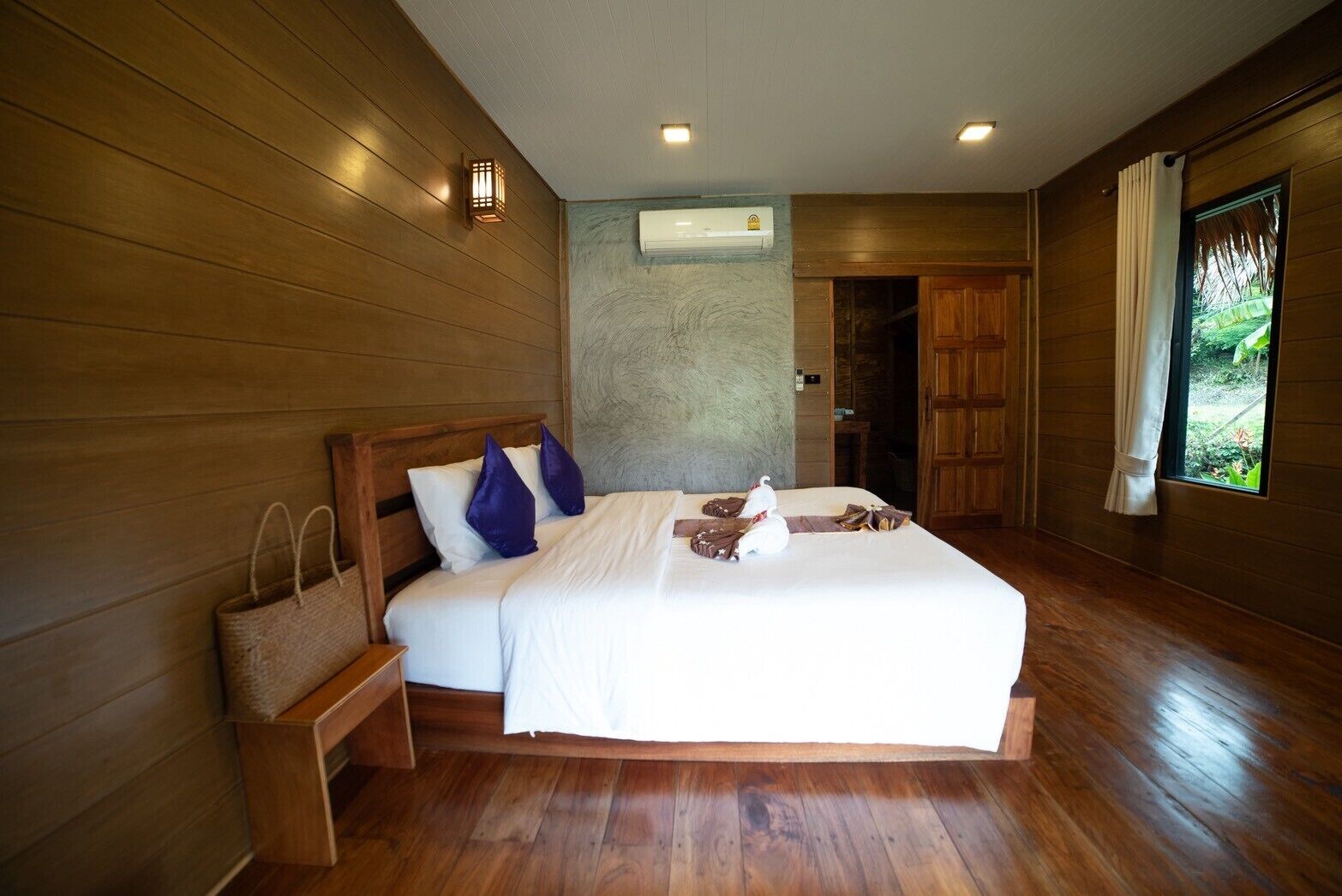 A bedroom with a wooden bed, white bedding, a nightstand, and a window with curtains.