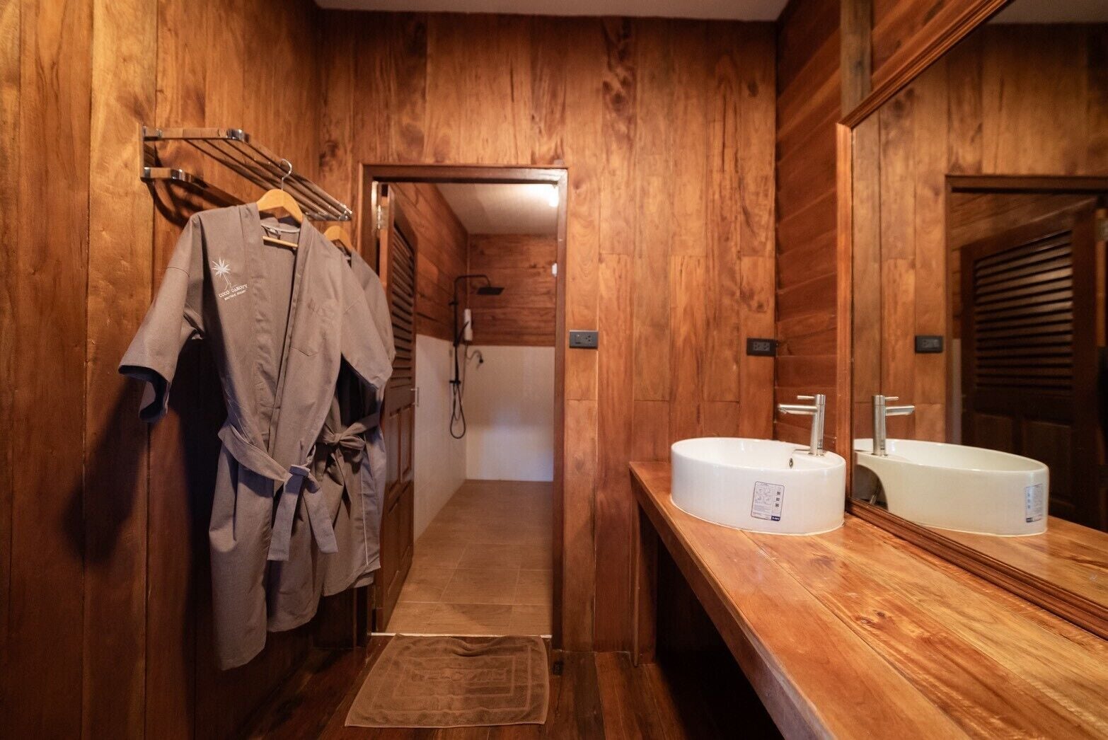 Une salle de bain en bois avec un grand miroir, deux lavabos et un peignoir suspendu à un porte-manteau.