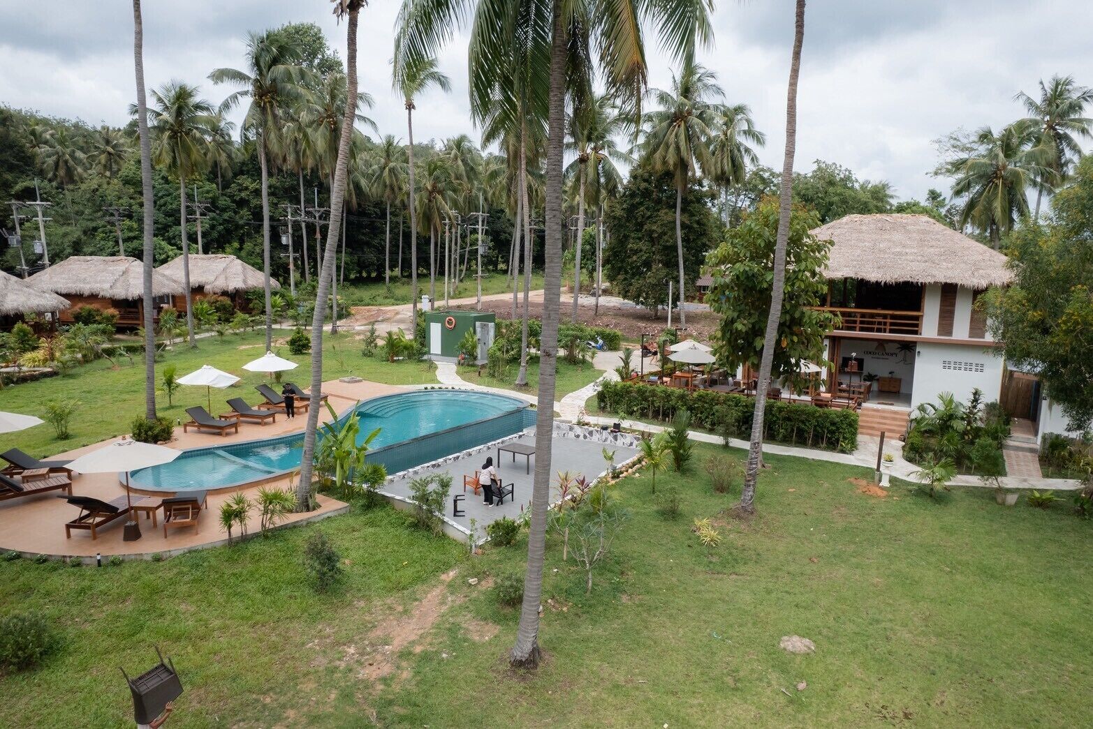 A resort with a swimming pool, lounge chairs, and thatched-roof structures.
