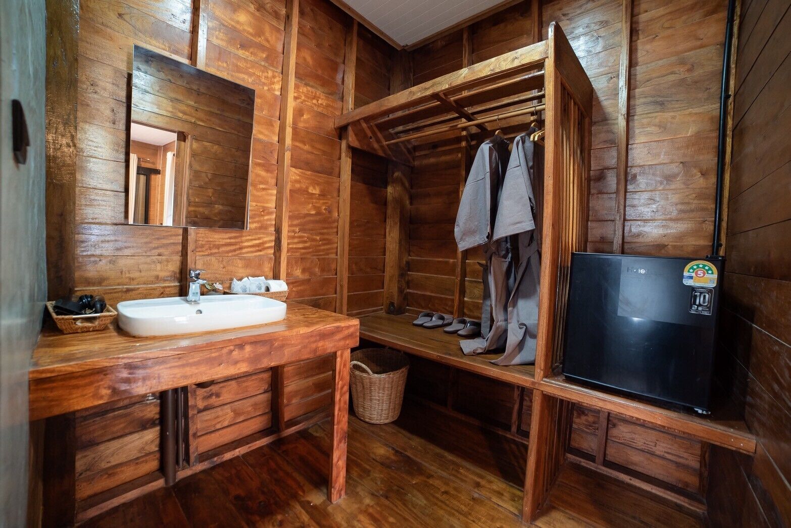 A wooden cabin bathroom with a sink, mirror, and a black refrigerator.