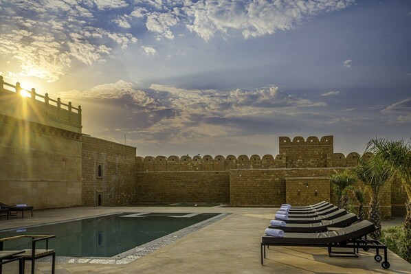 Una piscina con sillones de descanso, un muro de piedra y vista al cielo.
