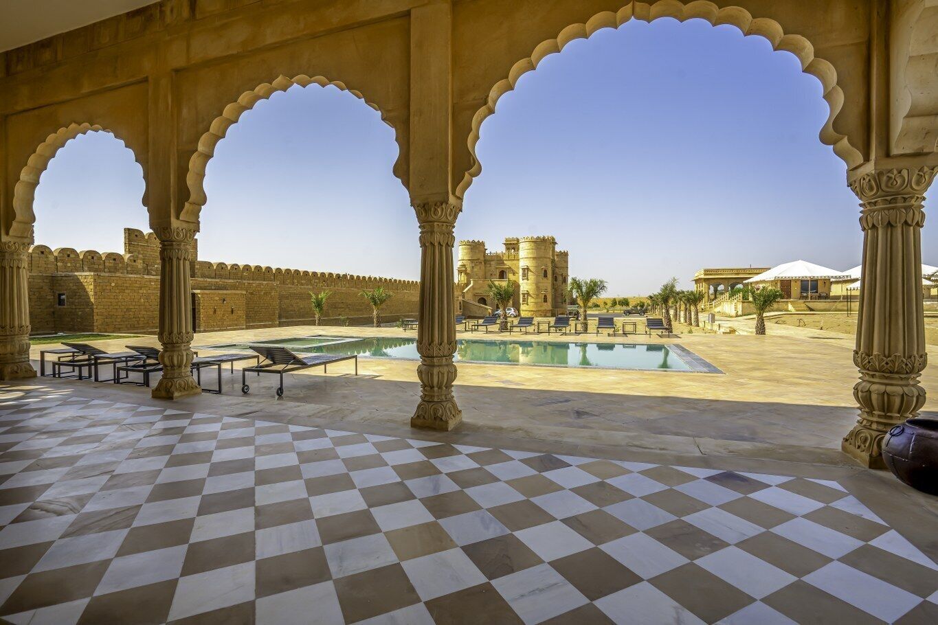 Un patio con suelo de cuadros, una piscina y vistas a una construcción que recuerda a un castillo.
