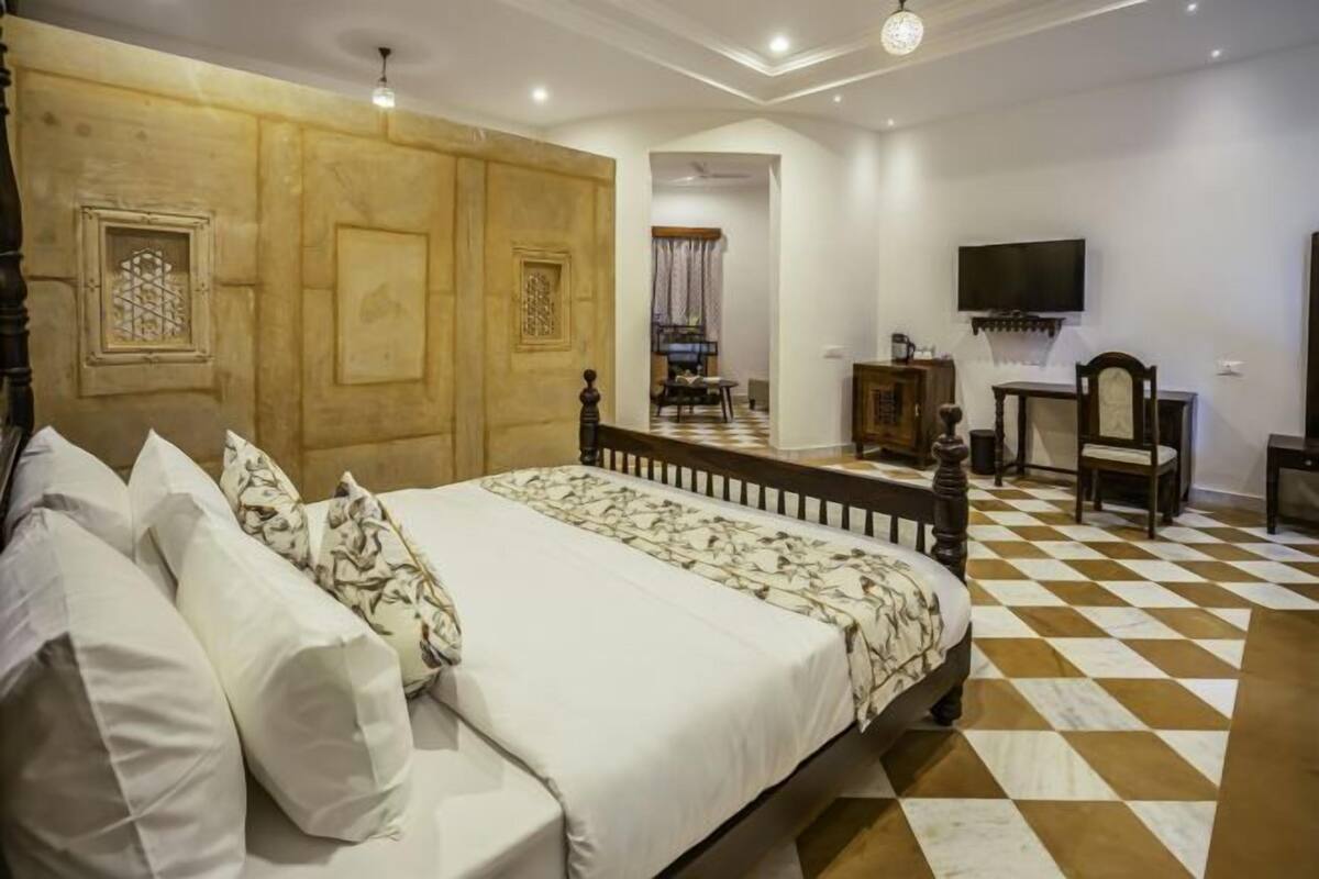 A bedroom with a large bed, a wooden headboard, a checkered floor, a television mounted on the wall, and a small table with a chair.