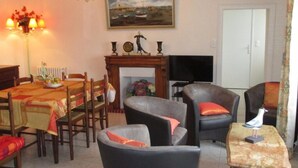 A dining area with a table set for four, surrounded by four chairs. There is a fireplace with a mantelpiece above it, and a television is mounted on the wall to the right. - Maison Ploubazlanec Pour 6 Personnes (Ploubazlanec)