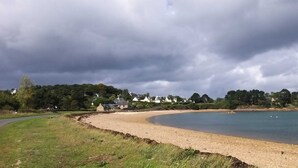 A coastal road curving along a beach with houses in the background. - Maison Ploubazlanec Pour 6 Personnes (Ploubazlanec)