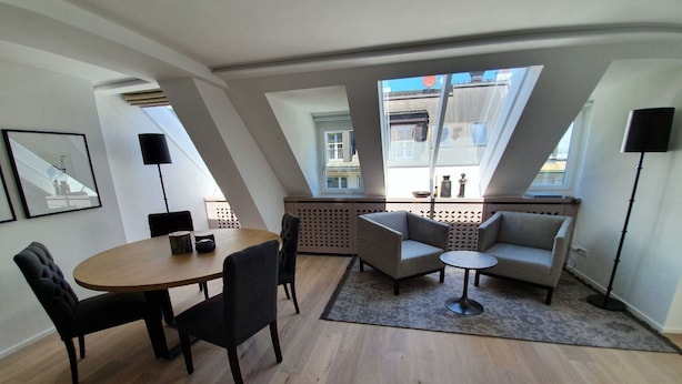 Ett modernt vardagsrum med en matplats, med ett runt bord, stolar, en soffa och ett litet soffbord. Stora fönster ger naturligt ljus och en fin utsikt över omgivningen.