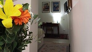 Un corridoio con una pianta in vaso, quadri appesi al muro e una zona pranzo sullo sfondo.