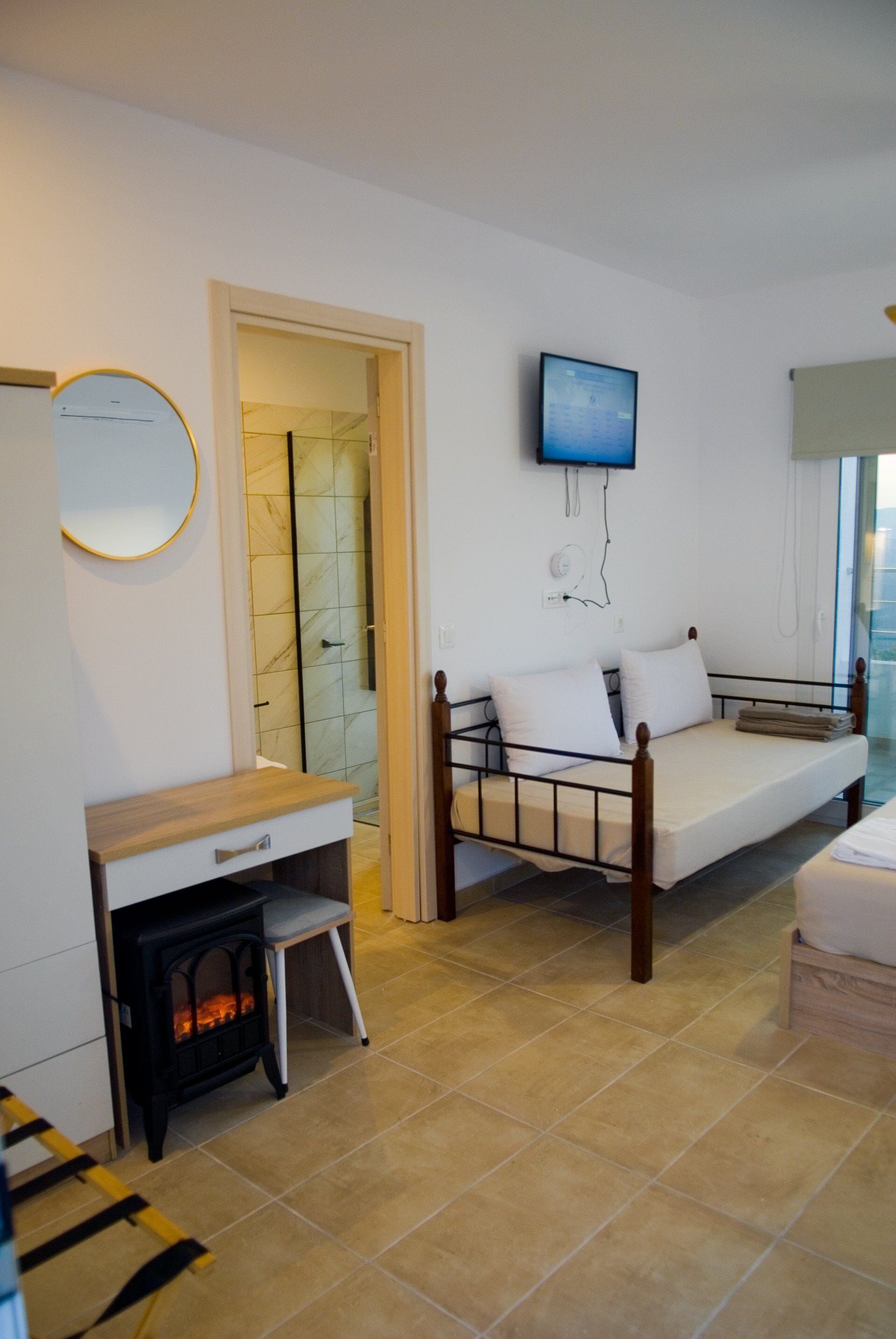 A bedroom with a bed, a TV mounted on the wall, a small wooden desk, and a fireplace.