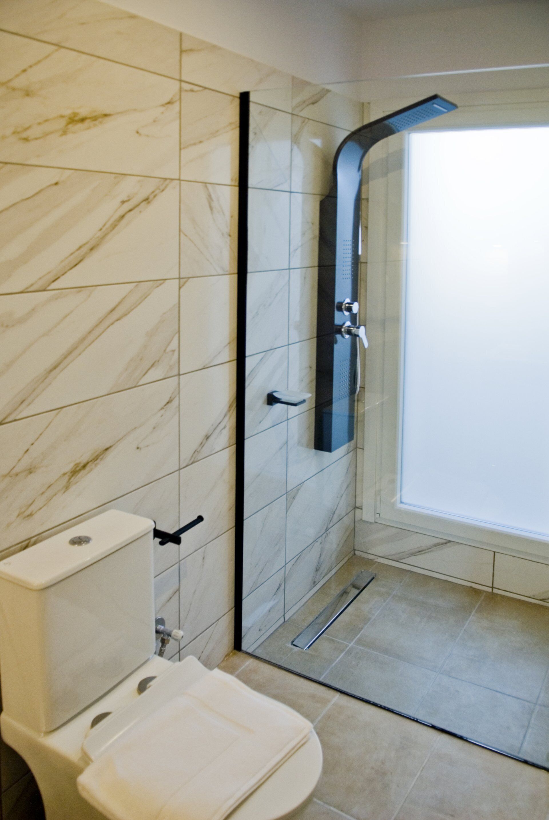 Une salle de bain comprenant des toilettes, une douche avec une porte en verre incurvée et des carreaux de marbre.