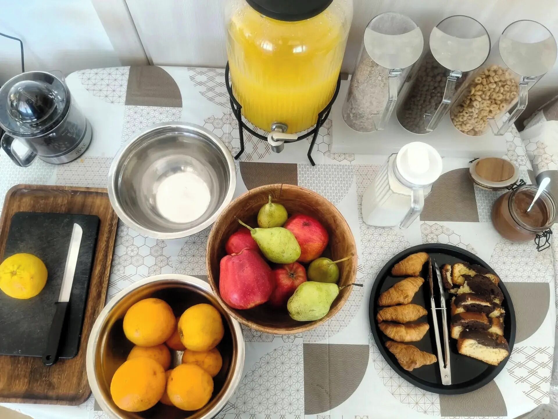 A breakfast table with various food items, a coffee maker, and a fruit bowl.
