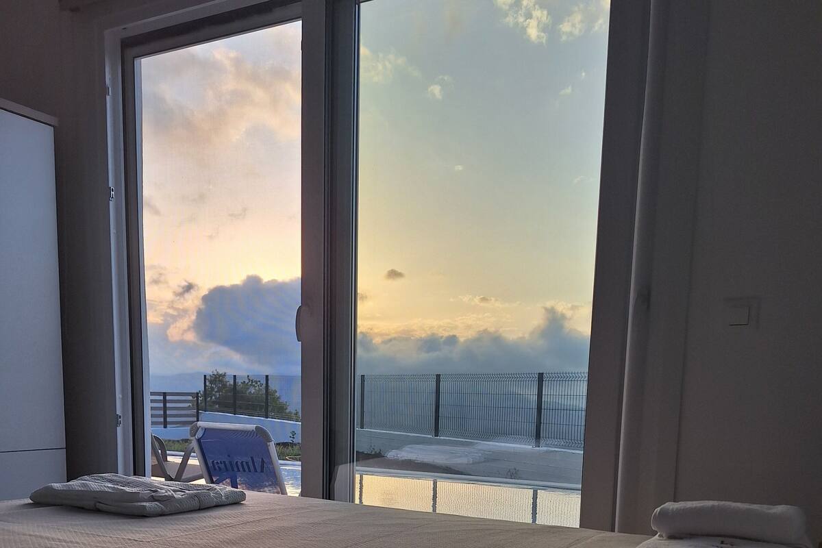 Een hotelkamer met een groot bed, een stoel en uitzicht op de lucht en een hek buiten.
