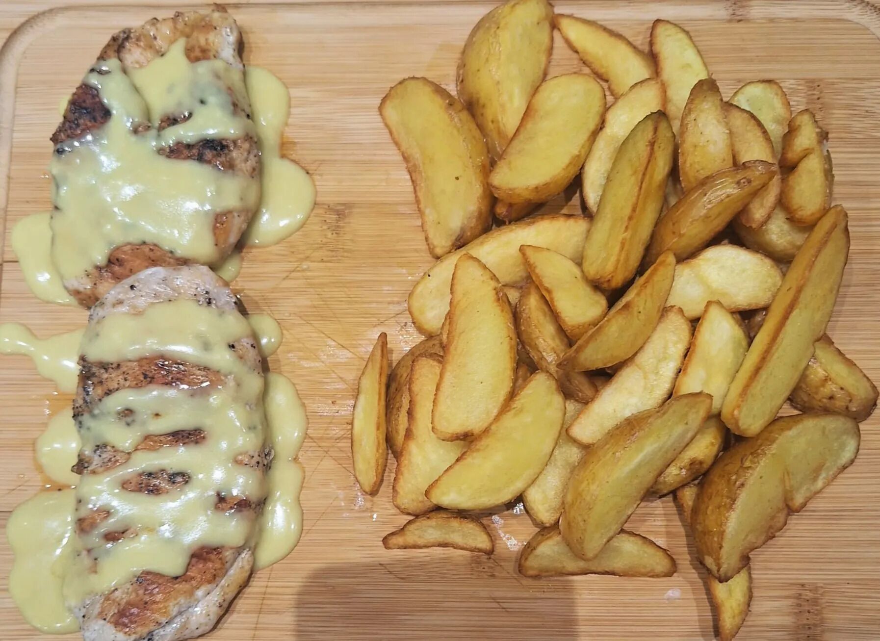 Una tabla de madera con pollo a la parrilla y una guarnición de papas asadas.