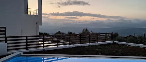 Un espace piscine extérieur moderne offrant une vue dégagée sur le paysage environnant et comprenant un bâtiment blanc doté d’un balcon.