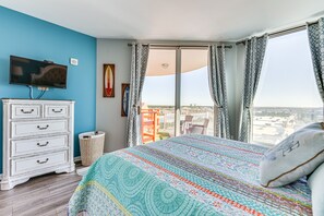 Une chambre avec un grand lit, une télévision, une commode et un balcon avec des rideaux.