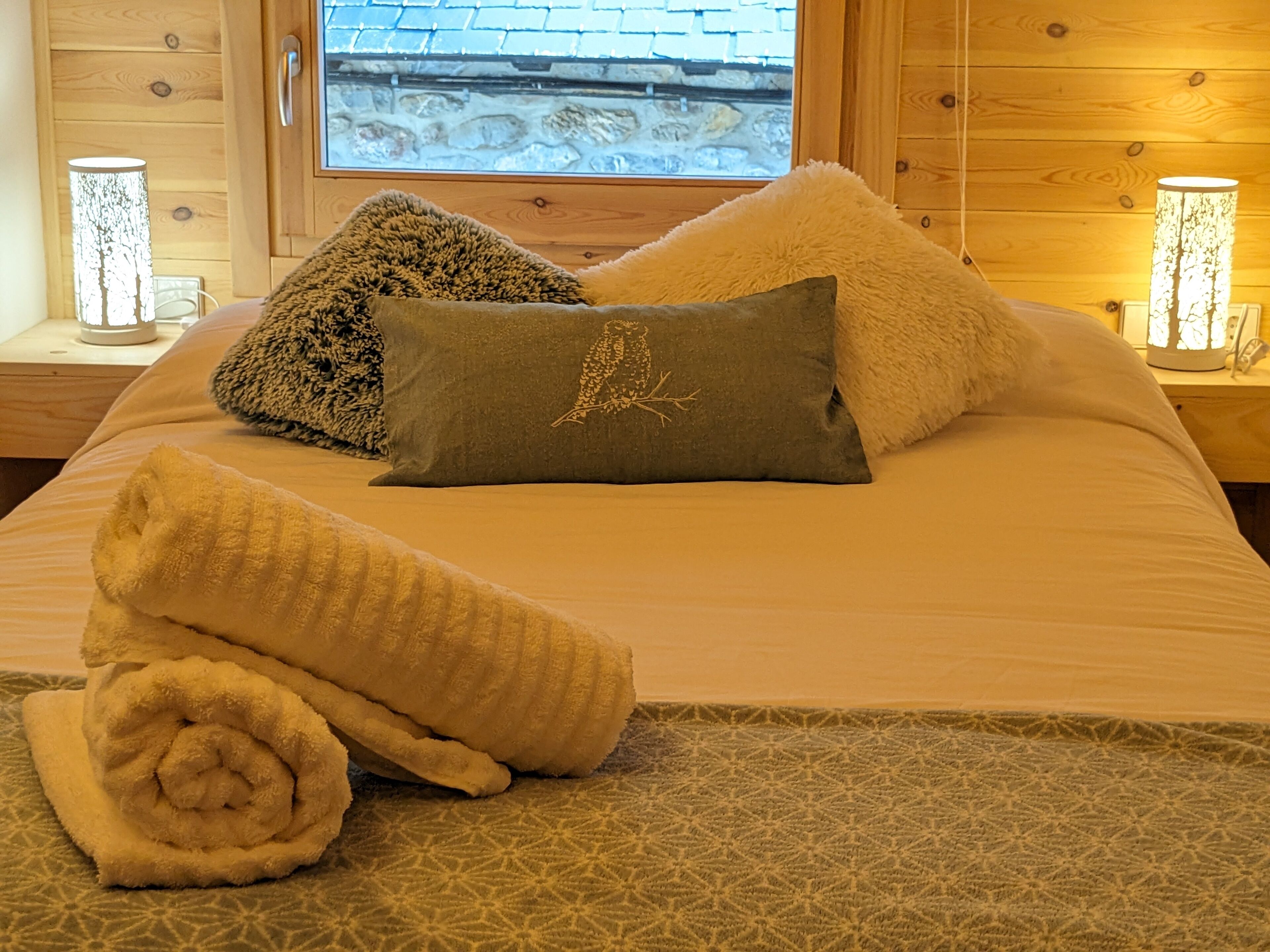 Ein ordentlich gemachtes Bett mit einem gemusterten Bettbezug, zwei Kissen und einem zusammengerollten Handtuch.