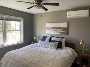 Relax in this serene bedroom with a large bed, ceiling fan, and air conditioning unit, surrounded by a beautiful landscape painting.