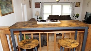 A rustic wooden dining table with two stools, a sofa, and a television in a cozy living room.