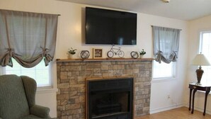 A living room with a stone fireplace, a mounted flat-screen TV, and a green armchair.