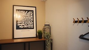 Ein gerahmtes Kunstwerk mit dem Titel 'ARTISAN FLORA' an der Wand, eine kleine Topfpflanze, ein hängender Laternenleuchter und ein Kleiderhaken mit Haken.
