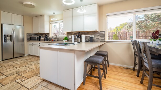 A modern kitchen with white cabinets, a stainless steel refrigerator, a large island with stools, and a window with a view of trees. - Santa Fe Retreat Near Railyard and Artsy Delights (Santa Fe)