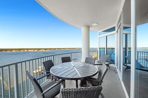 A balcony with a round table and wicker chairs, overlooking a body of water.