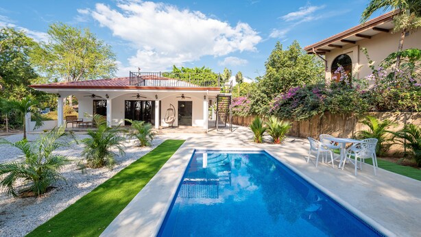 A backyard with a swimming pool, a covered patio, and a garden with various plants and trees. - Cozy beach house, partial view, 2 mn walk to beach (Guanacaste Province)