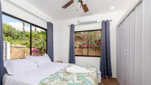 A bedroom with a bed, a ceiling fan, and a view of a garden through a window. - Cozy beach house, partial view, 2 mn walk to beach (Guanacaste Province)