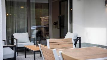 A modern outdoor seating area with a wooden table and two white chairs.
