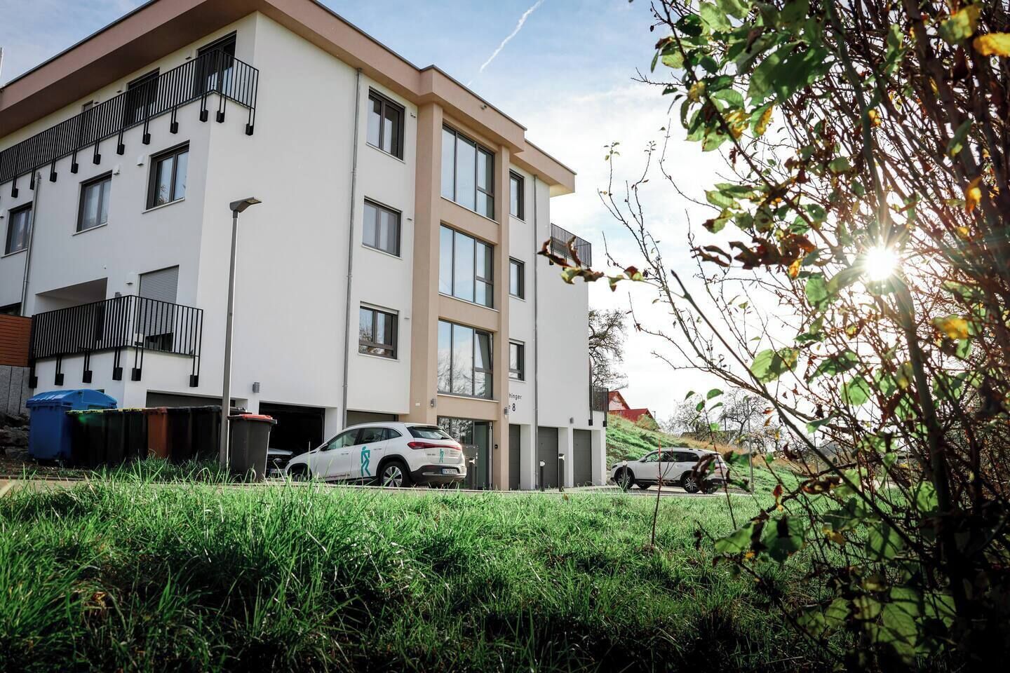 A modern multi-story building with a flat roof, large windows, and a balcony on the upper floors.