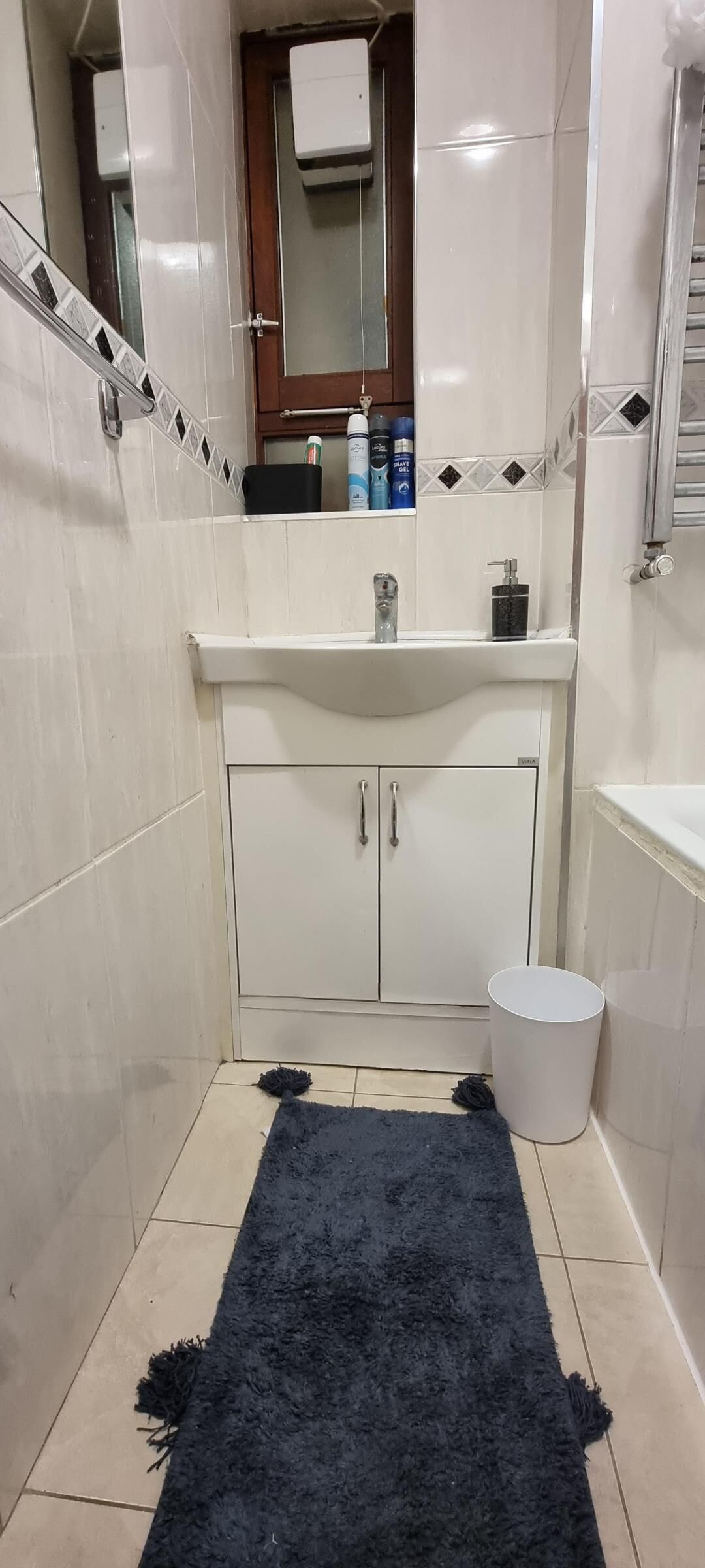 Kylpyhuoneessa on valkoinen pesuallas, peili ja kaappi. Lattialla on musta matto.
