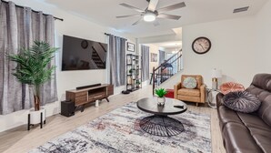 Uma sala de estar moderna com uma televisão de tela plana, um ventilador de teto, uma escada e um sofá de couro.