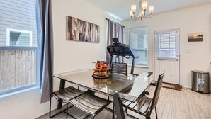 Uma sala de jantar com mesa de vidro, cadeiras de metal, lustre e obras de arte nas paredes.