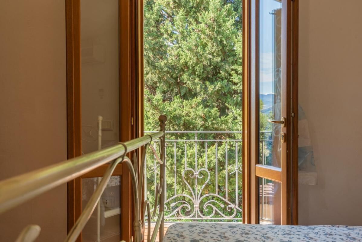 A bedroom with a balcony, a bed with a patterned bedspread, and a view of trees and mountains through the balcony.