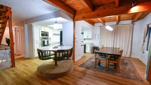 A spacious living area with a wooden ceiling, a round dining table, and a kitchen in the background. - Cozy and Artistic Space with a library and a Floating Net (Idaho Falls)
