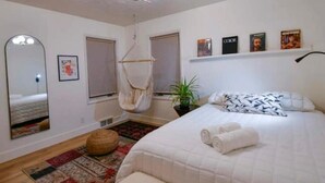 A bedroom with a bed, a hanging chair, a mirror, and a shelf with books. - Cozy and Artistic Space with a library and a Floating Net (Idaho Falls)