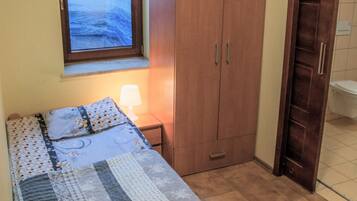 A bedroom with a bed, a wardrobe, a window, and a nightstand with a lamp.