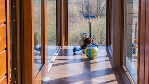 A hallway with wooden flooring and large windows, leading to a view of a scooter and a teddy bear. - NaFali (Kosakowo)