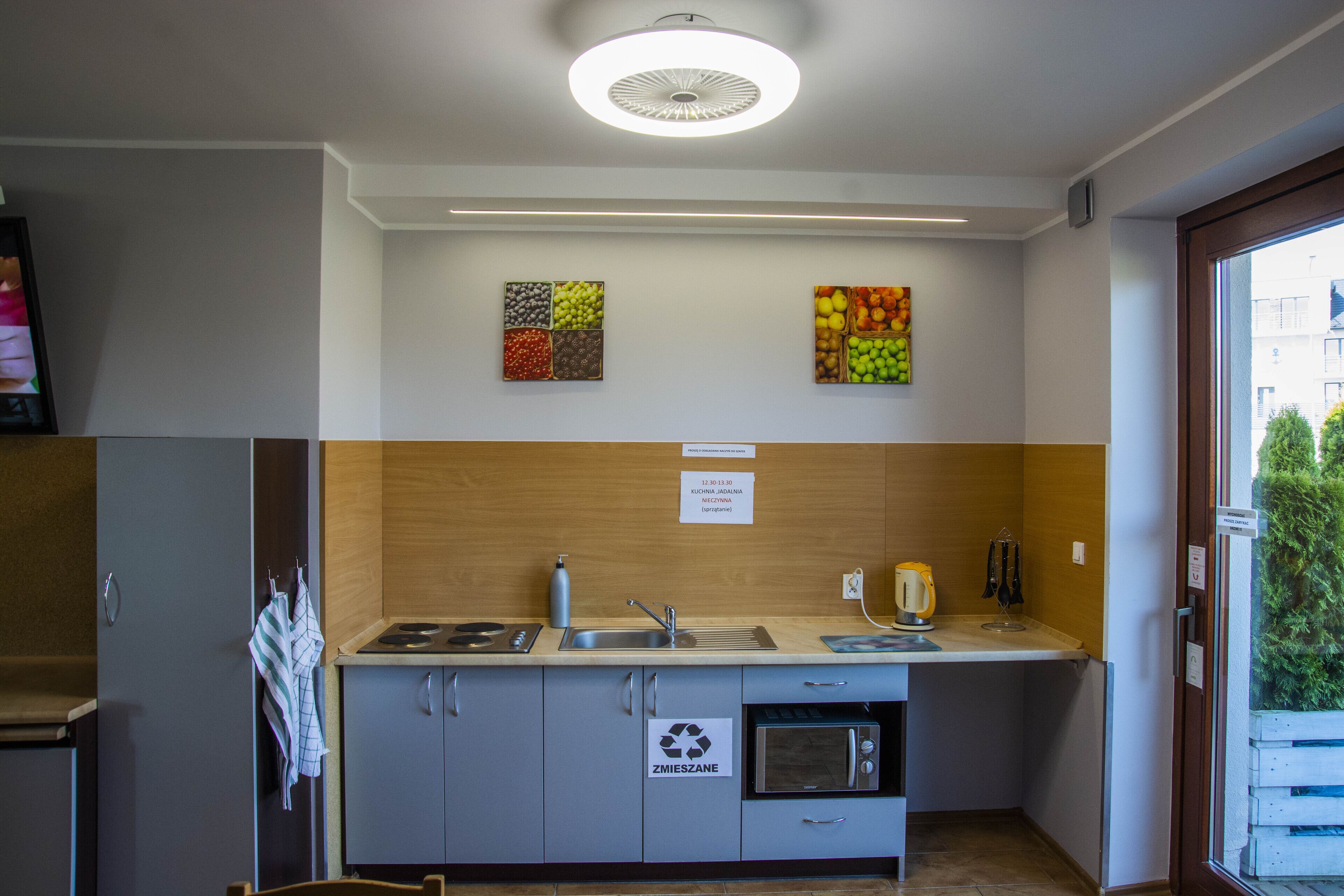 A modern kitchen with a sink, stove, and oven, wooden cabinets, and two fruit-themed wall art pieces.