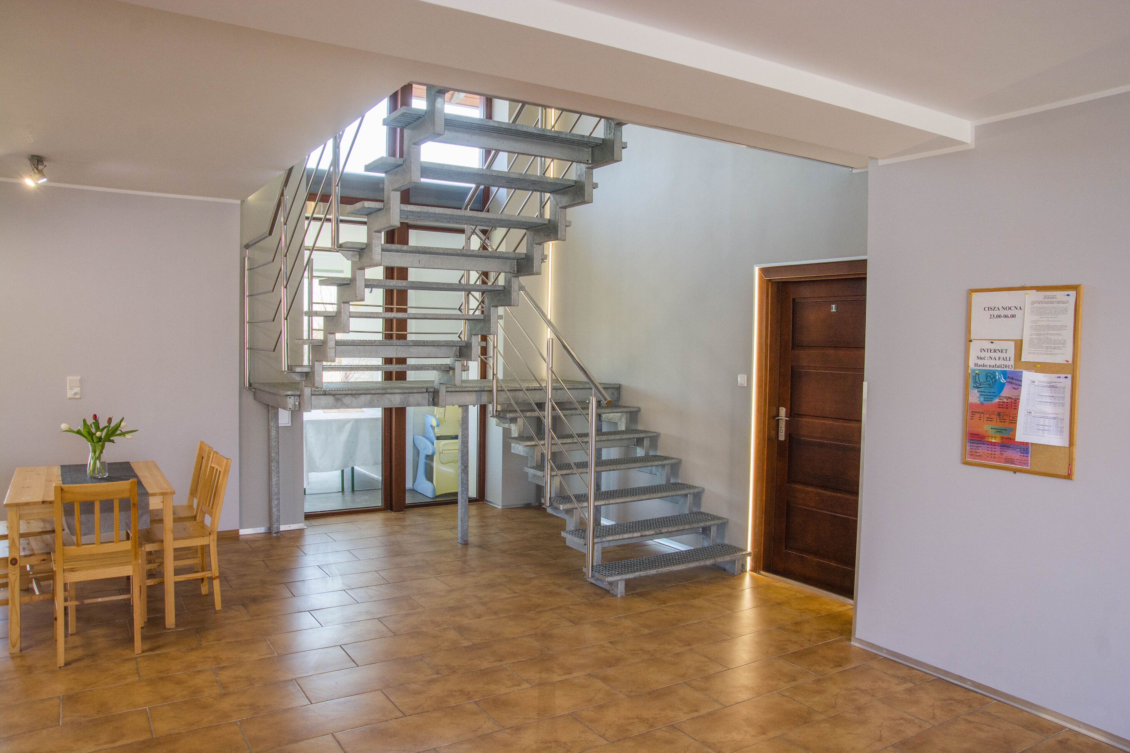 A modern interior with a spiral staircase, a wooden dining table, and a bulletin board.