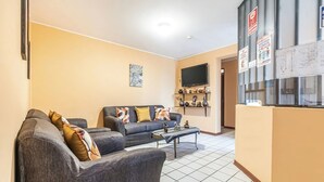 A living room with two grey sofas, a coffee table, and a flat-screen TV mounted on the wall. - Kurmi House Lima Airport (Callao)